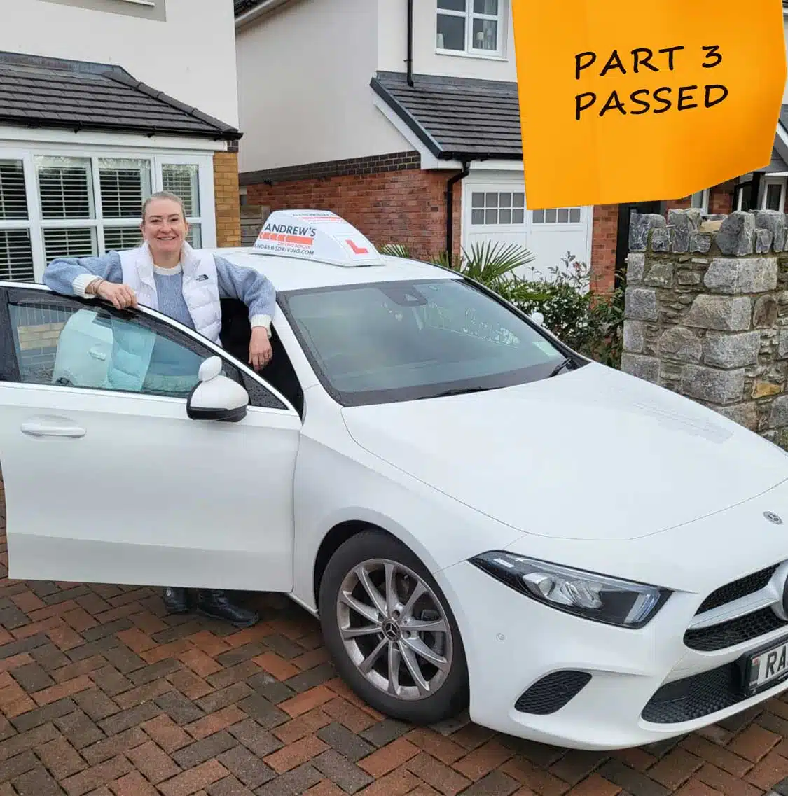 Julie Sheard celebrating passing Part 3 of her ADI test beside a white car