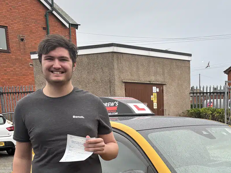 Newly passed James holding his pass certificate in front of his instructors car