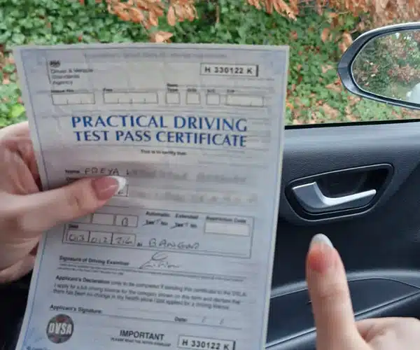 Hand holding a UK practical driving test pass certa thumbs-up gesture visible next to the document.