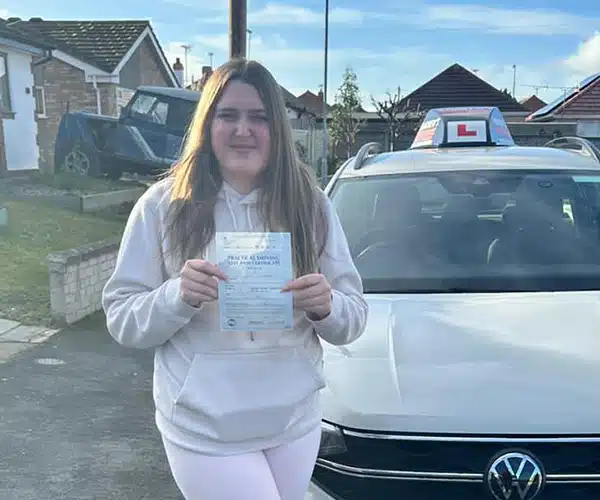 "Kaleigh smiling with her pass certificate in front of an Andrew's Driving School car"