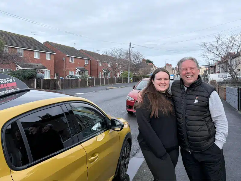 Paul Craft celebrating passing his ADI training course beside a yellow car