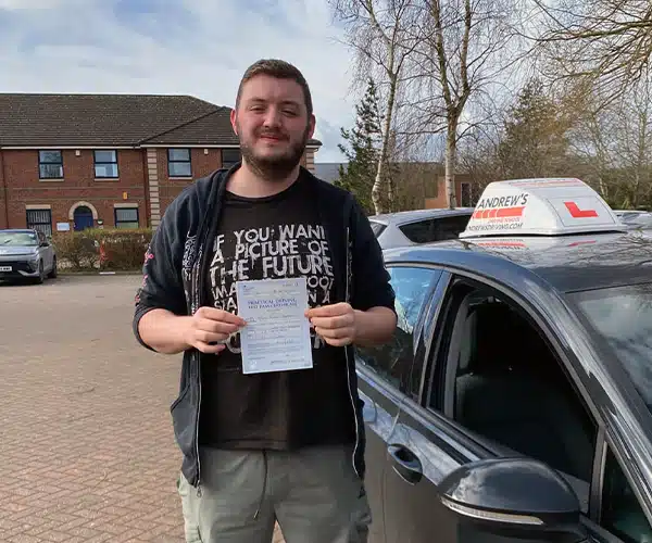 Adam celebrating a successful driving test pass inding his pass certificate beside the learner car.