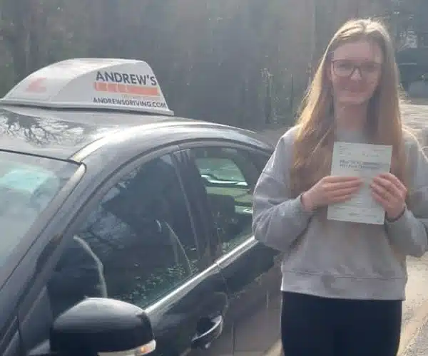 Isabella with her driving test pass certificate frtanding next to her instructors car in Colwyn Bay
