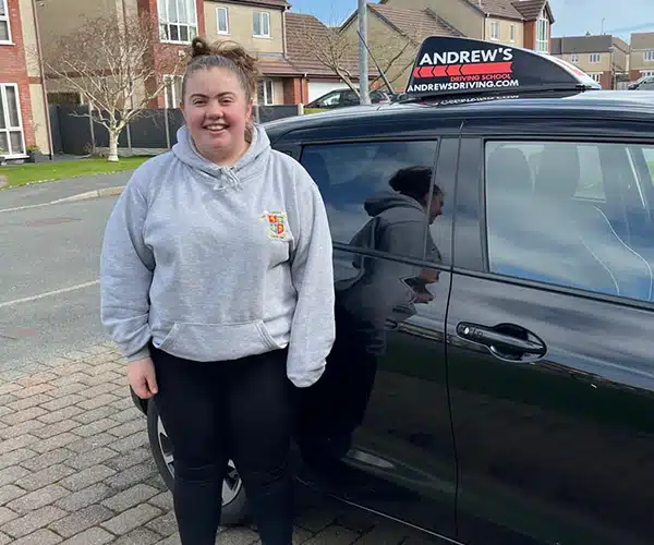 Smiling learner standing beside an Andrew’s Drivinidential street after passing their driving test.