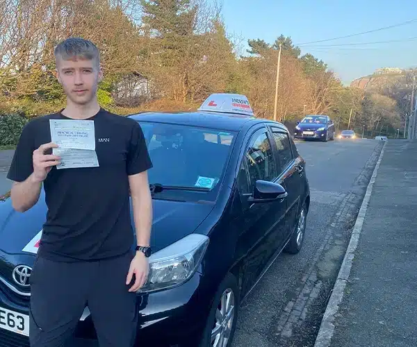 Lewis in Old Colwyn holding his driving test pass certificate beside Shane’s learner car. 🚗🎉