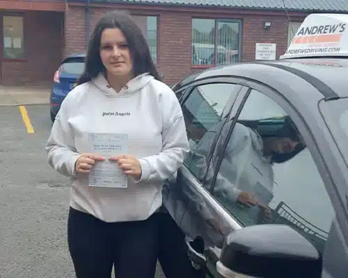 Maya Leece holding her driving test pass certificas driving school car at Rhyl Driving Test Centre.