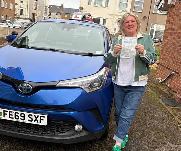 "Amanda stands beside Fiona's blue Toyota in Abergee, after passing at The Rhyl Driving Test Centre."