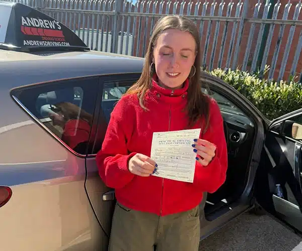 Caitlin holding her driving test pass certificate riving Test Centre beside instructor Ursula’s car