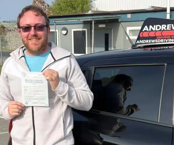 Chris holding his driving test pass certificate ator Driving Test Centre beside Llinos Begley’s car