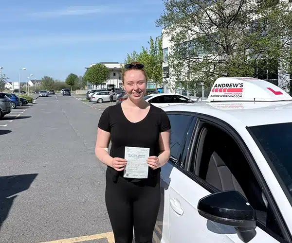 "Emily holding pass certificate beside Marcus's carNorth Wales Business Park Abergele on a sunny day"
