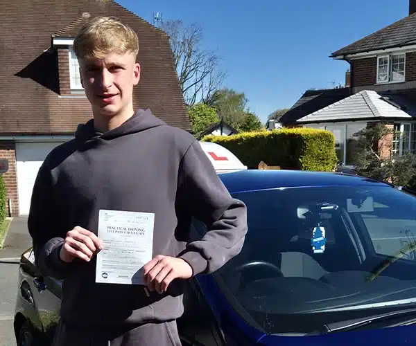 Evan holding his driving test pass certificate in Wrexham beside instructor Craig’s car