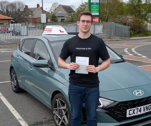 "Isaiah stands in front of Jack's green Hyundai at entre, holding his driving test pass certificate."