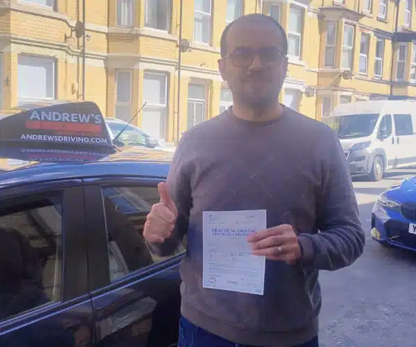 Khalid holding his driving test pass certificate nCentre after passing with Andrew’s Driving School