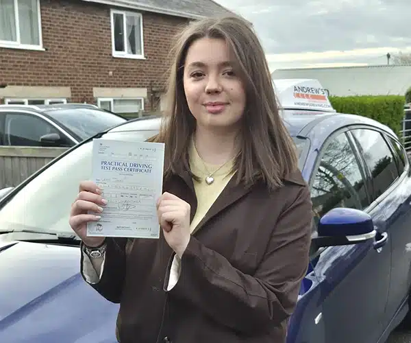 Leah holding her practical driving test pass certi the driving school car after passing in Wrexham.