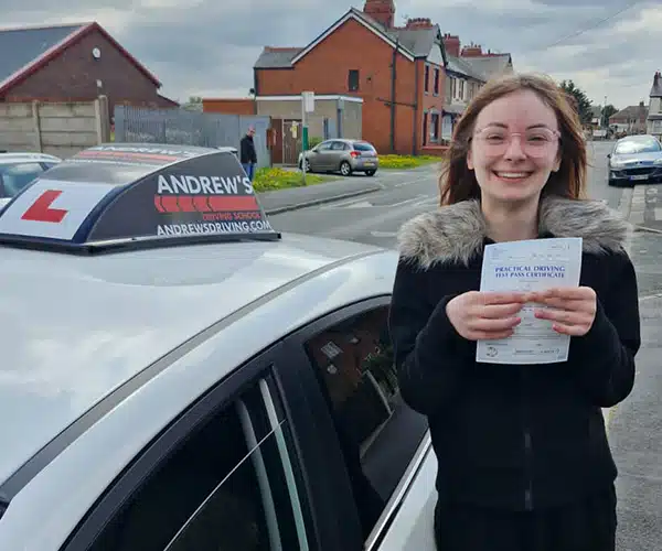 Misty holding her driving test pass certificate at Rhyl Driving Test Centre next to a learner car