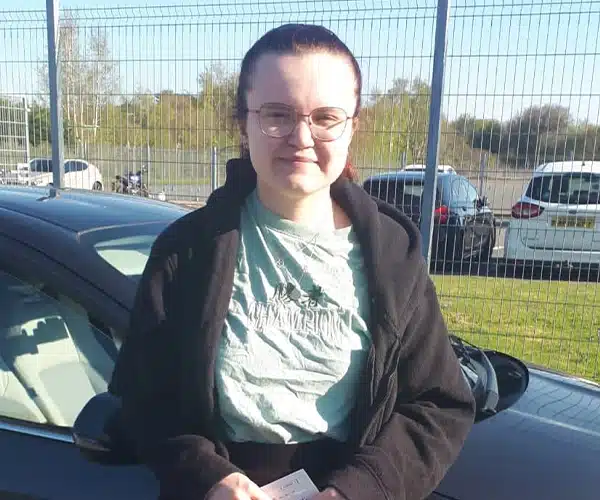 "Polly holding driving test pass certificate at Ban Driving Test Centre beside Barry's automatic car"