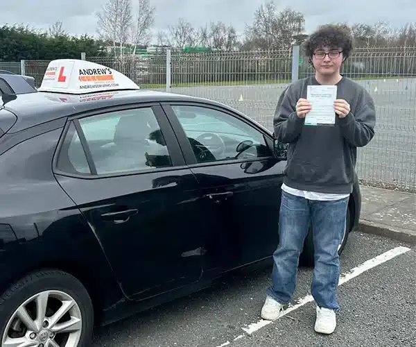 Tiago from Holyhead holding his practical driving ner car in Bangor after passing his driving test.