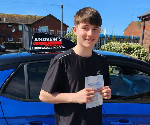 Zac Hewitt holding driving test pass certificate aiving Test Centre next to blue driving school car